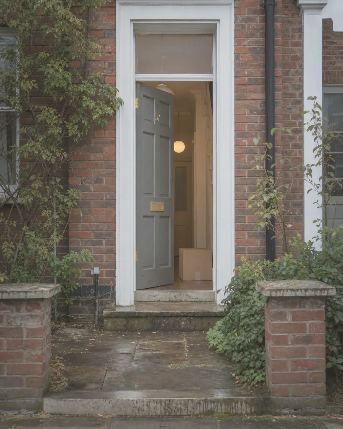 An open front door on a wet afternoon, hall light on, a packing box just inside